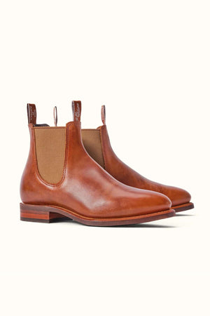 The RM Williams Moriarty Rubber Sole Boot is a pair of brown pull-up leather Chelsea boots with elastic side panels and pull tabs, featuring an almond toe, smooth finish, and a low wooden heel for added comfort.