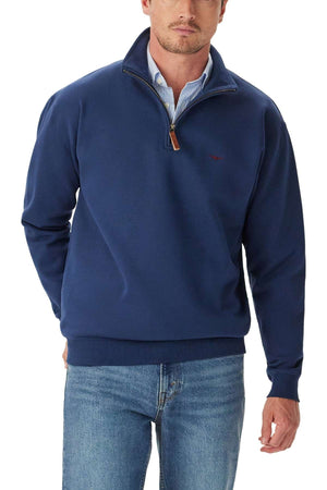 Man wearing the RM Williams Mulyungarie 1/4 Zip Sweatshirt in navy blue over a light blue collared shirt and blue jeans, standing with one hand in his pocket against a white background.