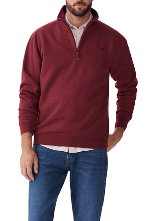 Someone wears an RM Williams Mulyungarie Fleece in maroon over a striped dress shirt and blue jeans. The fleece has a small embroidered logo on the chest, with one hand casually tucked in their pocket.