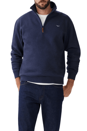 A man in a RM Williams Mulyungarie Fleece, navy blue brushed cotton quarter-zip sweatshirt with a small white logo on the chest, paired with dark jeans. He wears a white shirt underneath and casually rests his hands in his jean pockets. His head is cropped out of the image.