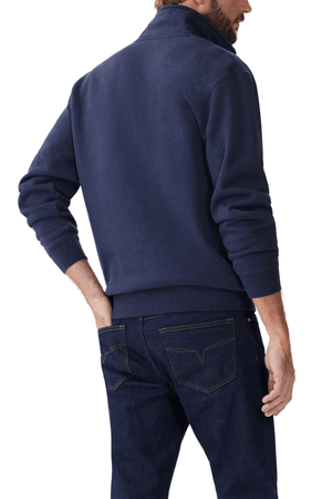 A man wears the RM Williams Mulyungarie Fleece, a dark blue quarter-zip sweatshirt, paired with denim jeans. Captured from the side and back, the image showcases this casual brushed cotton fleece outfit, with his hand in a pocket.