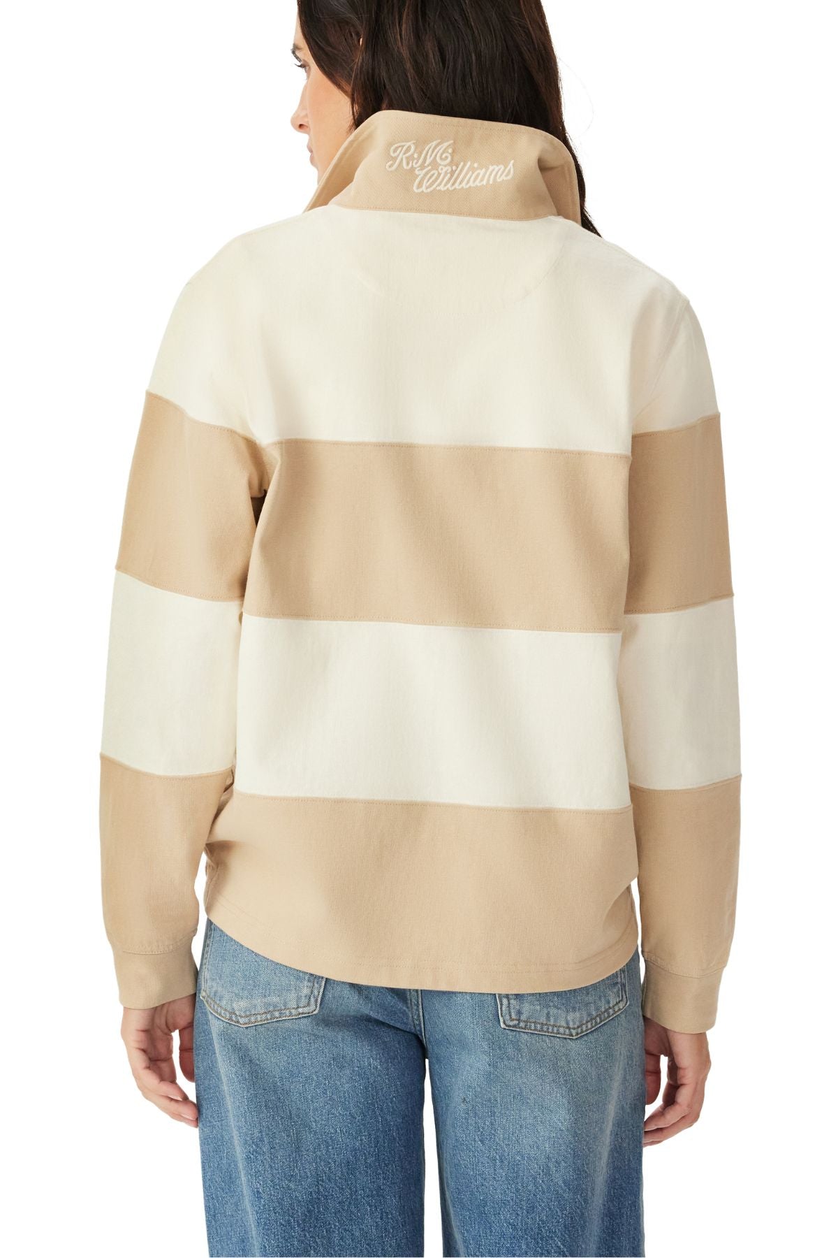 Woman shown from the back wearing the RM Williams Narran 4 Panel Rugby, a beige and white striped jacket with "R.M. Williams" embroidered on the collar, paired with blue jeans.
