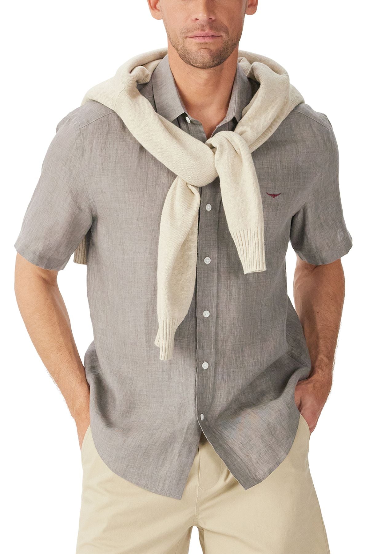 A man wears the RM Williams Newman Linen Short Sleeve Shirt in light gray with a cream sweater draped over his shoulders, paired with light beige pants. His hands are in his pockets.