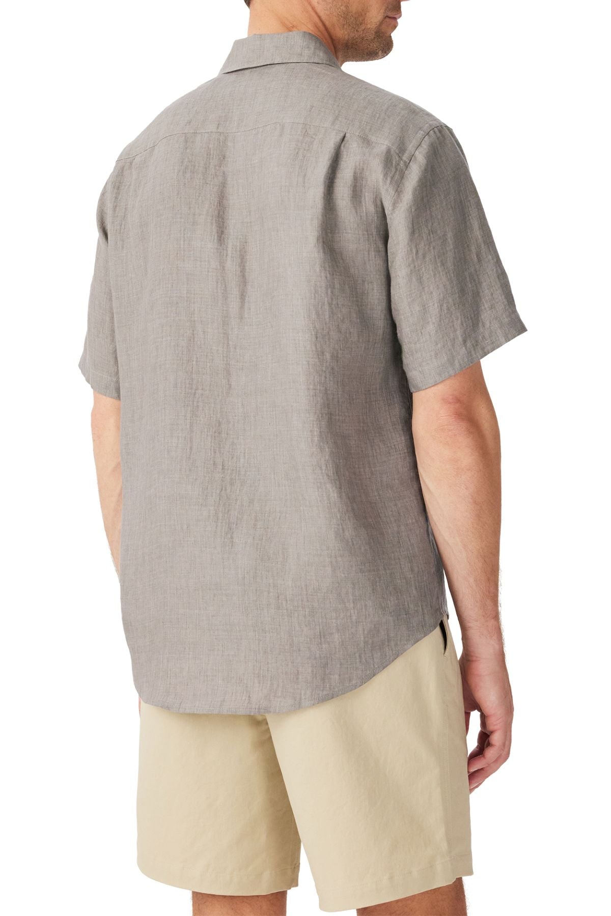 A man is seen from behind wearing the RM Williams Newman Linen Short Sleeve Shirt in light gray with beige shorts. The untucked shirt has a relaxed fit and lightweight French linen fabric, showing his upper body and part of his legs.