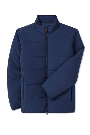 The RM Williams Padstow Jacket is a navy blue, lightweight puffer made from recycled nylon. It has Primaloft fill, a high collar, a full-length zipper, horizontal stitching, and elastic cuffs, with one sleeve partially folded over the body.
