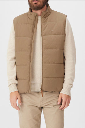 A man wears the RM Williams Padstow Vest—a beige puffer made from recycled nylon—over a light beige sweater and beige pants. He stands with arms relaxed at his sides against a plain background, head partially out of frame.