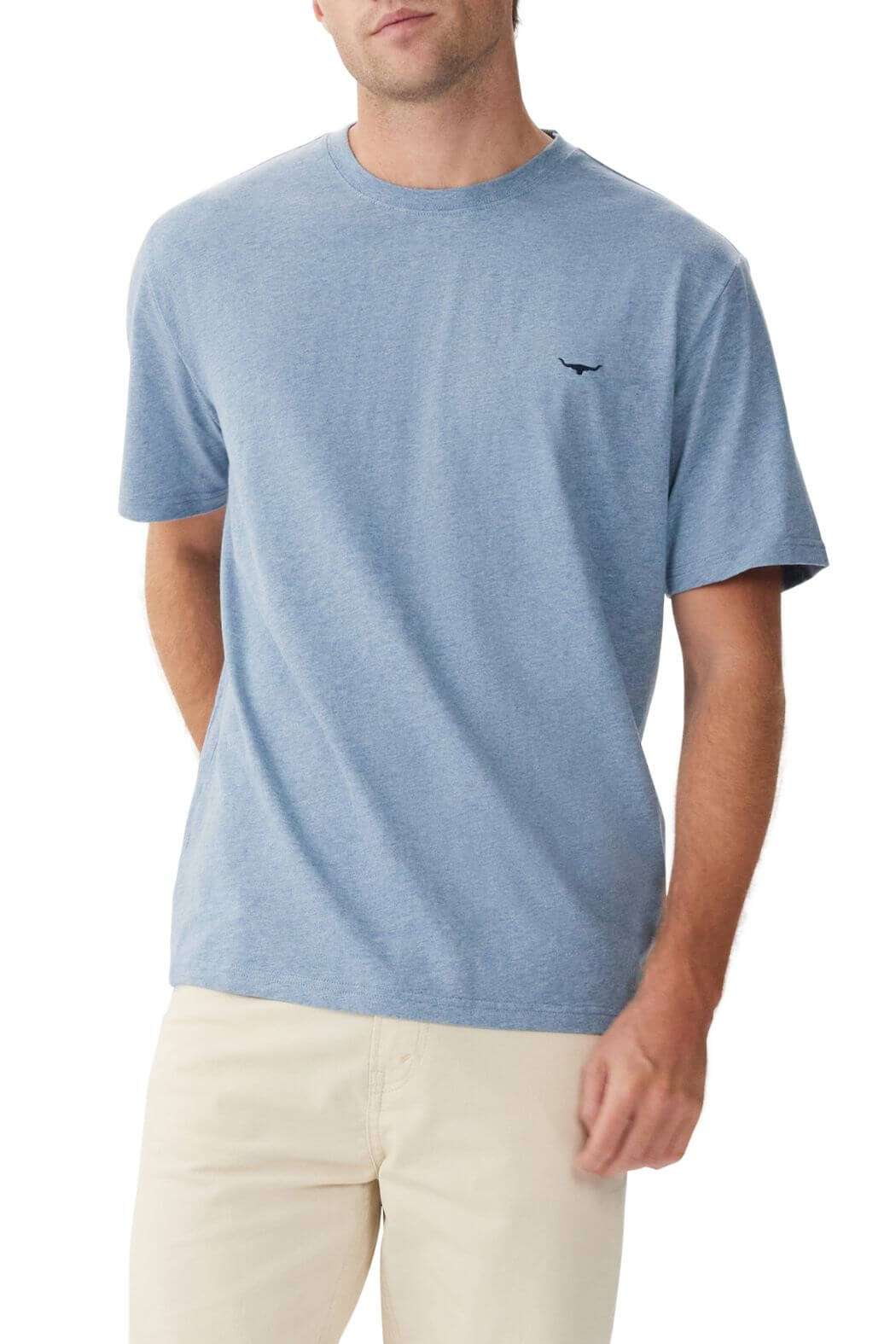 Dressed in a light blue RM Williams Parson T-Shirt made from breathable cotton, featuring a small longhorn embroidery on the chest, the person pairs it with beige pants, set against a plain white background with arms partly behind their back.