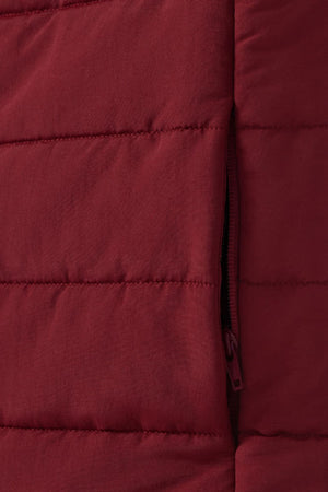 Close-up of the quilted maroon fabric, likely from the RM Williams Patterson Creek Vest. The image shows horizontal stitching and a partially visible side zipper pocket, suggesting it's a stylish yet functional water-resistant puffer vest.