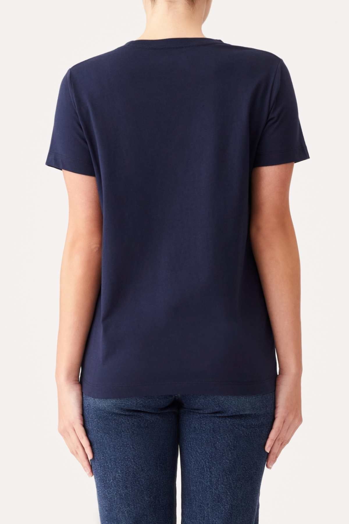 A person facing away from the camera is wearing an RM Williams Piccadilly T-Shirt made of organic cotton and dark blue jeans. The background is plain and light-colored.