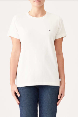 A person stands against a plain background, wearing an RM Williams Piccadilly T-Shirt and blue jeans. The white short-sleeved organic cotton T-shirt features a small, dark-colored Longhorn embroidery on the upper left side. The individual stands with arms relaxed at their sides.