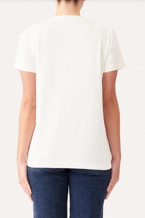 A person stands facing away from the camera, wearing a plain white RM Williams Piccadilly T-Shirt and blue jeans. The background is a simple, solid off-white color. The person's arms are relaxed by their sides.