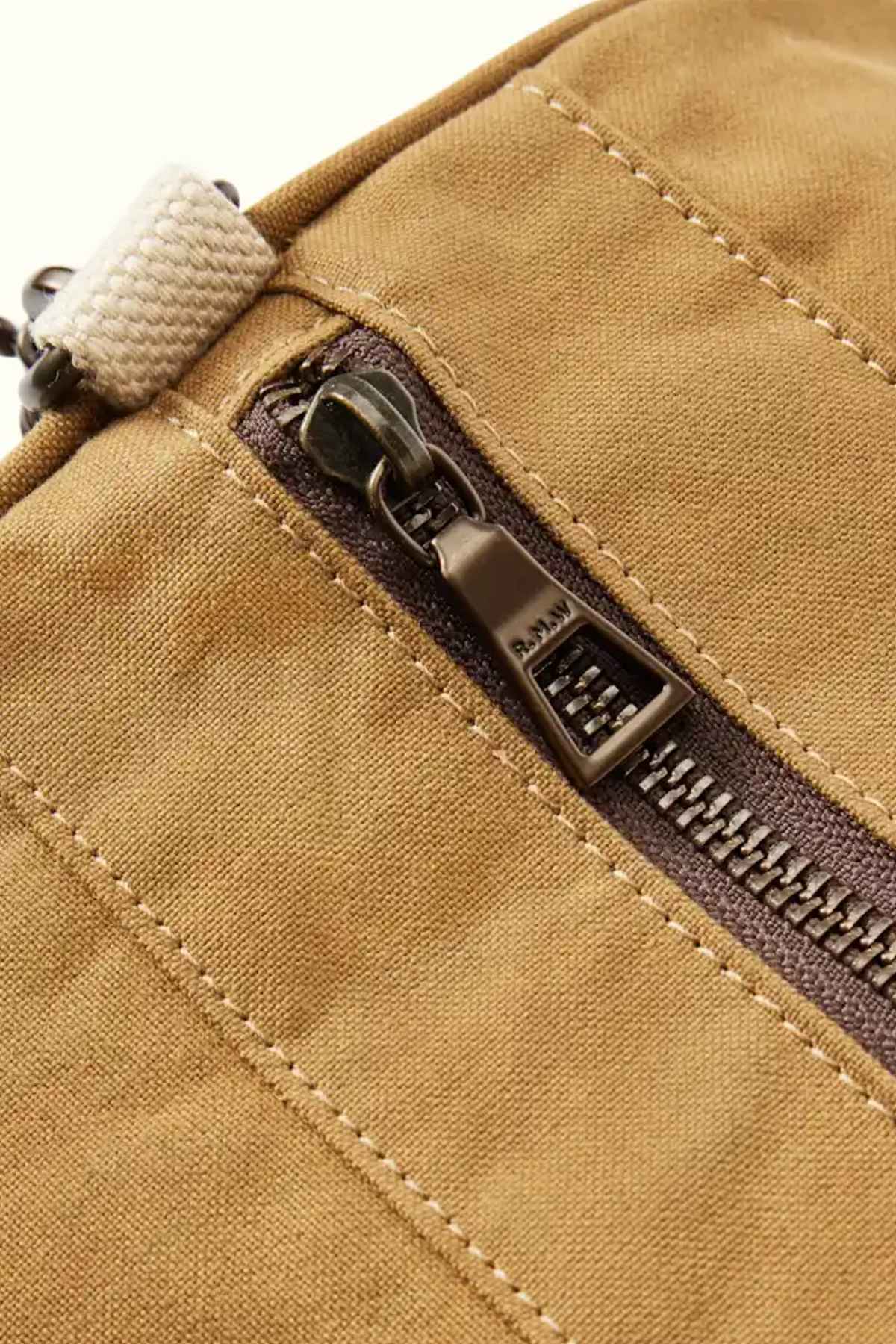 Close-up of the RM Williams RM Ditty Bag, a brown fabric accessory with a metallic zipper, partially open to showcase its intricate stitching details. Made from waxed cotton canvas, it includes an adjustable crossbody strap and a small beige handle at the top corner, making it the perfect travel companion.