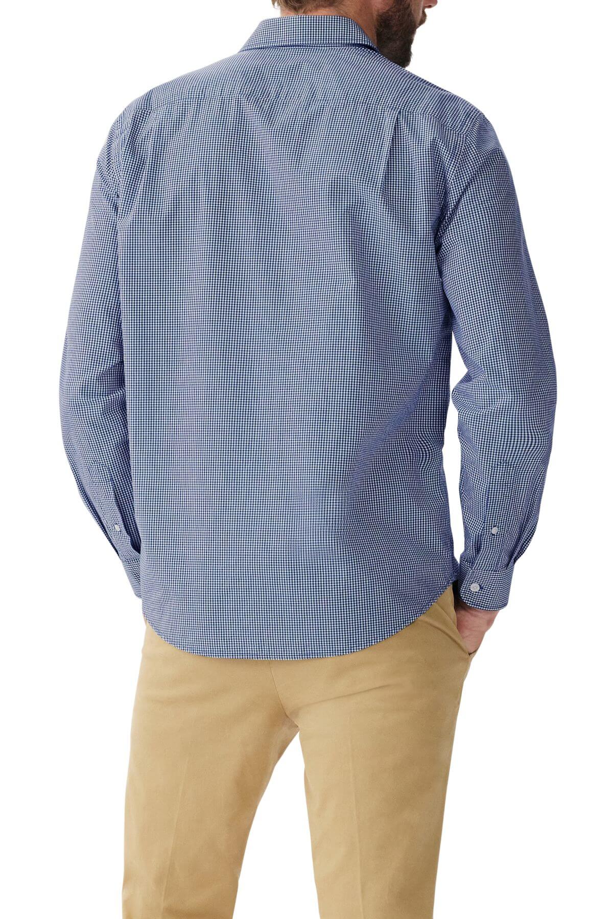 A man with a beard is seen from behind, wearing the RM Williams Classic Shirt in blue micro gingham check and beige pants. He has one hand in his pocket. The regular fit shirt, crafted from organic cotton, features long sleeves and a collar.
