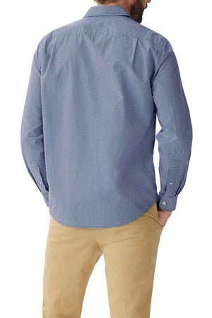 A man with a beard is seen from behind, wearing the RM Williams Classic Shirt in blue micro gingham check and beige pants. He has one hand in his pocket. The regular fit shirt, crafted from organic cotton, features long sleeves and a collar.