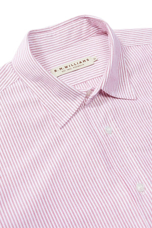 A close-up of the RM Williams Regular Shirt, featuring light pink and white stripes, a collared button-down style, and a medium "R.M. Williams" tag. Made from organic cotton for comfort in a slim regular fit.