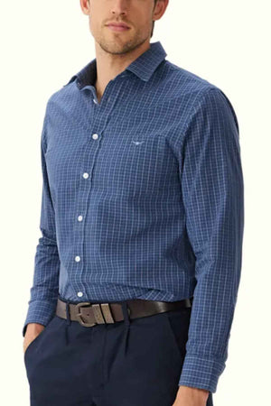 A person in an RM Williams Regular Shirt featuring a blue, long-sleeved, slim fit design with a checkered pattern and an Oxford cotton button-down collar stands with one hand in a pocket. They are wearing dark pants and a black belt against a plain white background.