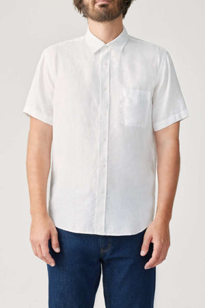 A person wearing the RM Williams Regular Short Sleeve Shirt, a short-sleeved button-up made from organic cotton with a pocket, paired with dark blue jeans. The background is plain gray.