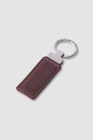 The RM Williams Ridgewood Key Fob is crafted from brown Moulton leather with visible stitching, features a silver metal key ring, and is embossed with the signature R.M. Williams logo for timeless style and quality.