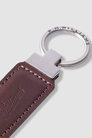 Close-up of the RM Williams Ridgewood Key Fob featuring brown Moulton Leather with visible stitching, an embossed R.M. Williams logo, and a metal edge engraved with “R.M. WILLIAMS” for a refined finish.