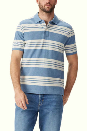 A man is wearing the RM Williams Rod Polo made from breathable cotton pique, featuring horizontal white stripes and a collar. Paired with blue jeans, he poses against a plain background with one arm hanging loosely by his side.