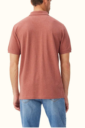 A person stands with their back to the camera, wearing the RM Williams Rod Polo in red, made from organic cotton pique, paired with blue jeans against a plain background.