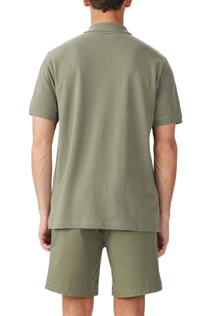 A man stands with his back to the camera in a matching olive green RM Williams Rod Polo organic cotton pique short-sleeve shirt and shorts set, set against a plain white background.