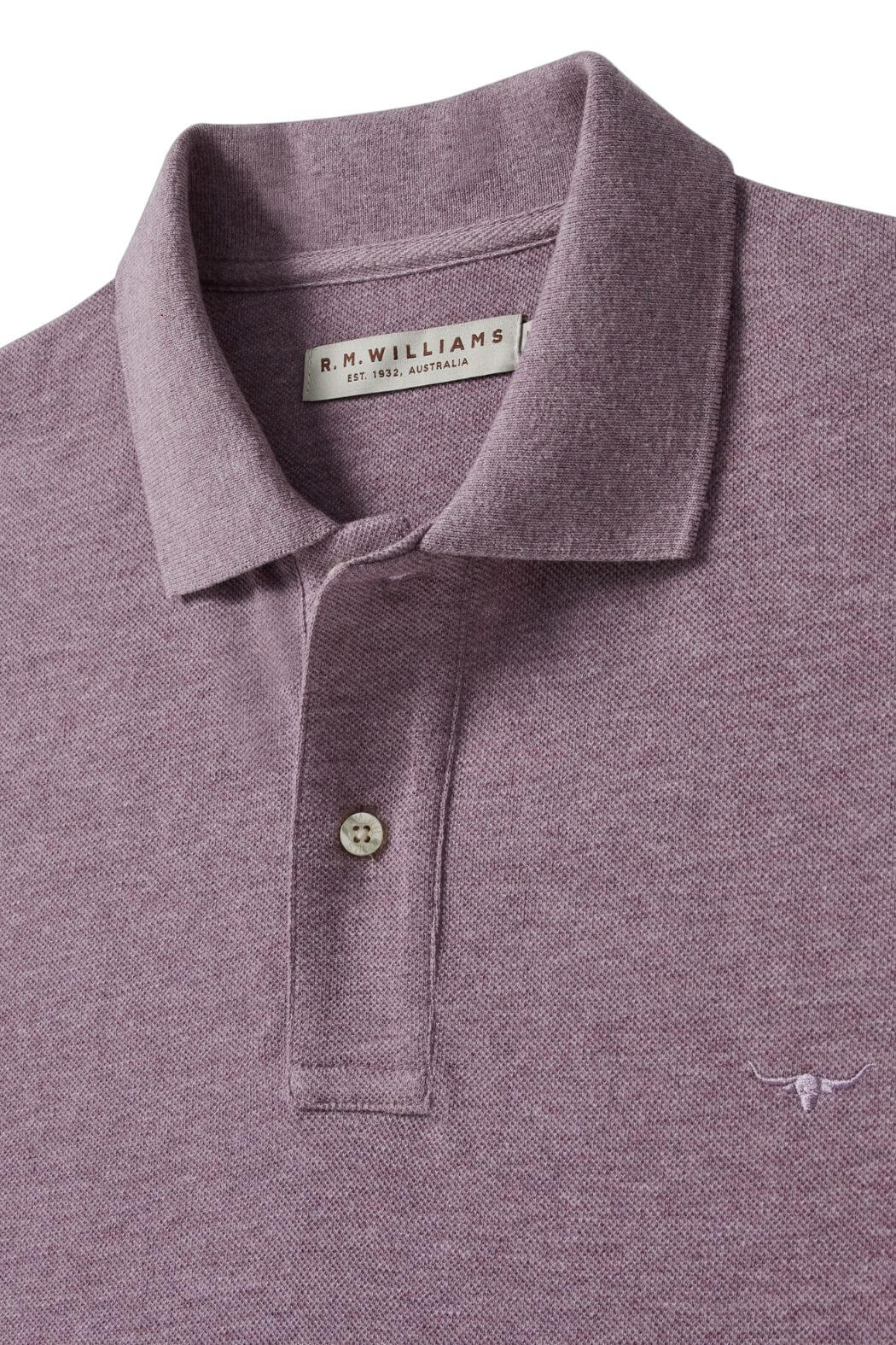 A close-up of the mauve RM Williams Rod Polo showcases its folded collar, two-button placket, small longhorn chest embroidery, and visible brand label inside the collar. The shirt is crafted from breathable cotton pique fabric.