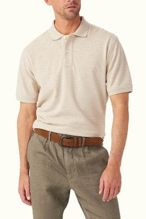 A man sports the RM Williams Rod Polo, a classic fit in beige crafted from breathable organic cotton pique. It is neatly tucked into gray trousers and complemented by a brown belt, with the ensemble standing out against a plain white background.