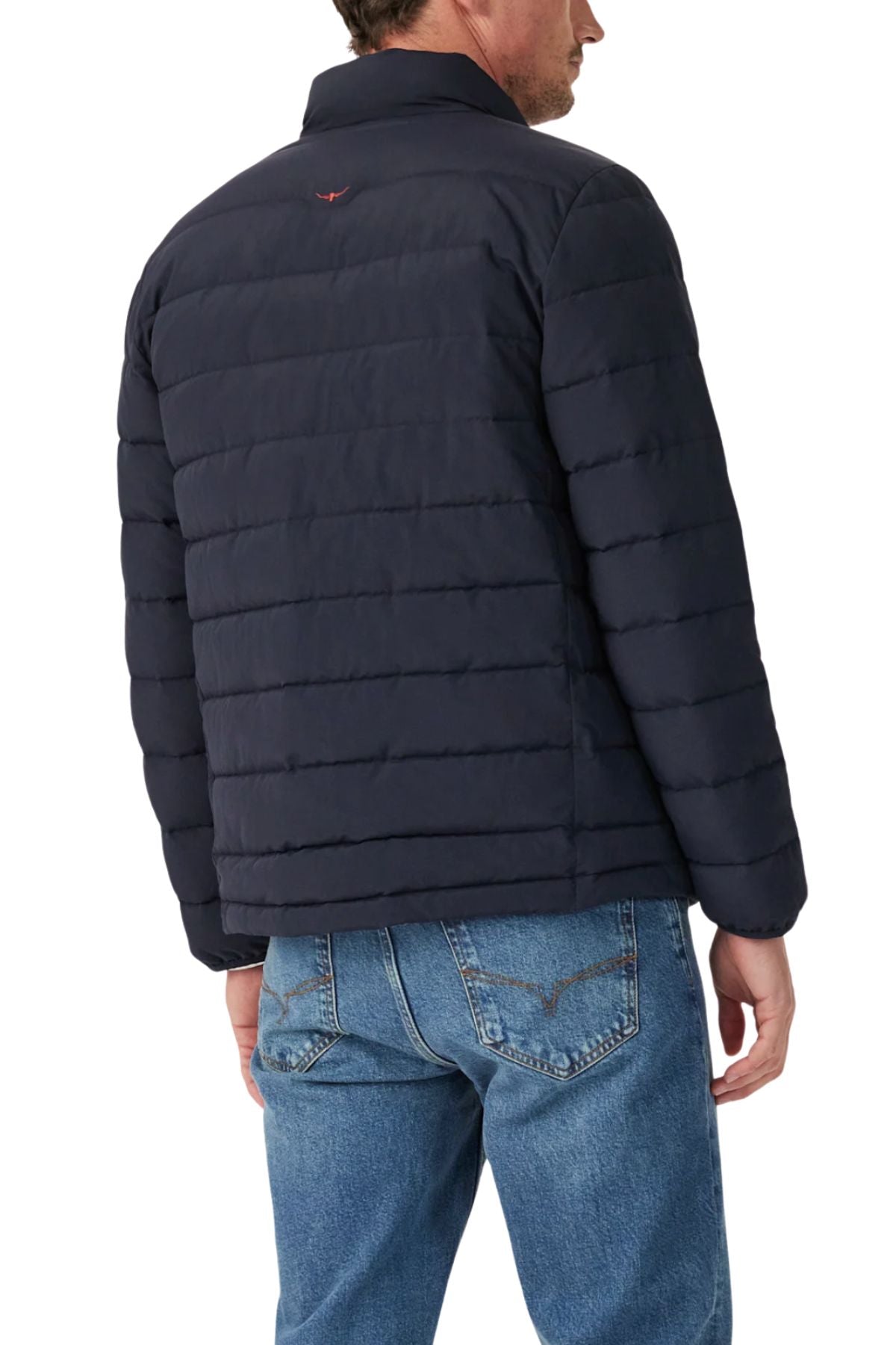 A man wearing the RM Williams Rydal Padded Jacket in navy blue and blue jeans stands with his back to the camera against a white background.