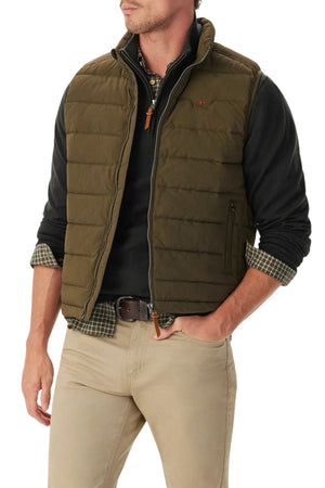 A man wears the RM Williams Rydal Padded Vest in green over a black pullover and plaid shirt, teamed with beige pants. With one hand in his pocket, he gives this cozy, layered look a stylish edge for cooler days.
