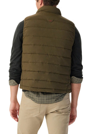 A man is shown from the back wearing the RM Williams Rydal Padded Vest in green over a dark long-sleeve shirt and checked shirt, paired with beige pants. His sleeves are rolled up and his hands rest at his sides.