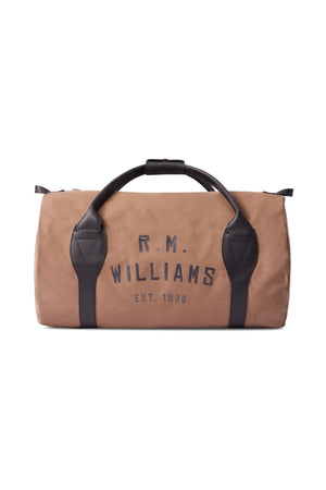 The RM Williams Sorrento Ute Bag is a tan canvas duffel with black leather trims and handles, boldly featuring "R.M. Williams EST. 1932" on the front. Made in Australia for lasting style and durability.