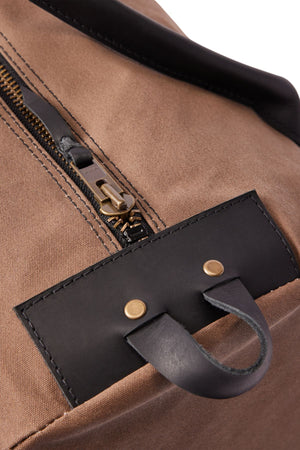 Close-up of the RM Williams Sorrento Ute Bag in brown Utility Canvas with a gold zipper, black leather trims, and a leather pull tab secured by two brass rivets. Made in Australia.