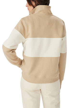 A person wearing the RM Williams Trickett Panel Sweatshirt, a beige and white colorblock design with a high collar and wide white horizontal stripe across the upper back and arms, paired with light-colored pants.