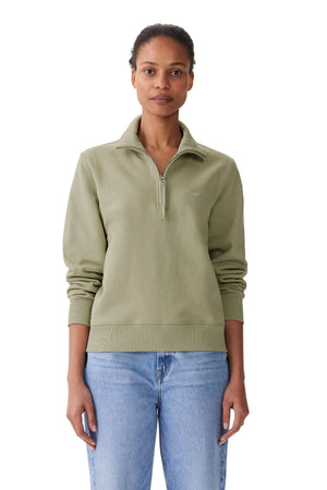 A person stands facing forward wearing a RM Williams Trickett Zip Neck Sweatshirt in light green with longhorn embroidery, paired with blue jeans. The cotton terry fabric enhances comfort against a clean white background.