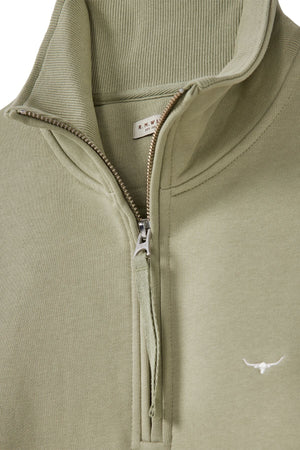 A light olive green RM Williams Trickett Zip Neck Sweatshirt in cotton terry, featuring a high collar, half-zip design, and subtle white longhorn embroidery on the lower front.