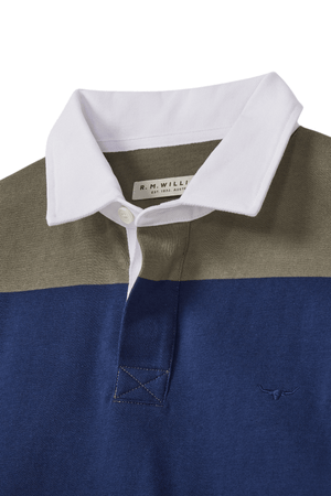 A close-up of the RM Williams Tweedale Rugby shows its heavyweight jersey knit, white collar, olive green upper, and blue lower section with a small longhorn embroidery logo on the blue chest fabric.