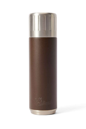 The RM Williams Vacuum Flask is sleek and brown with a textured stainless steel body, metallic accents, and engraved text. It features double wall vacuum insulation and has a polished screw-on lid. The flask's cylindrical design stands upright against a white background.