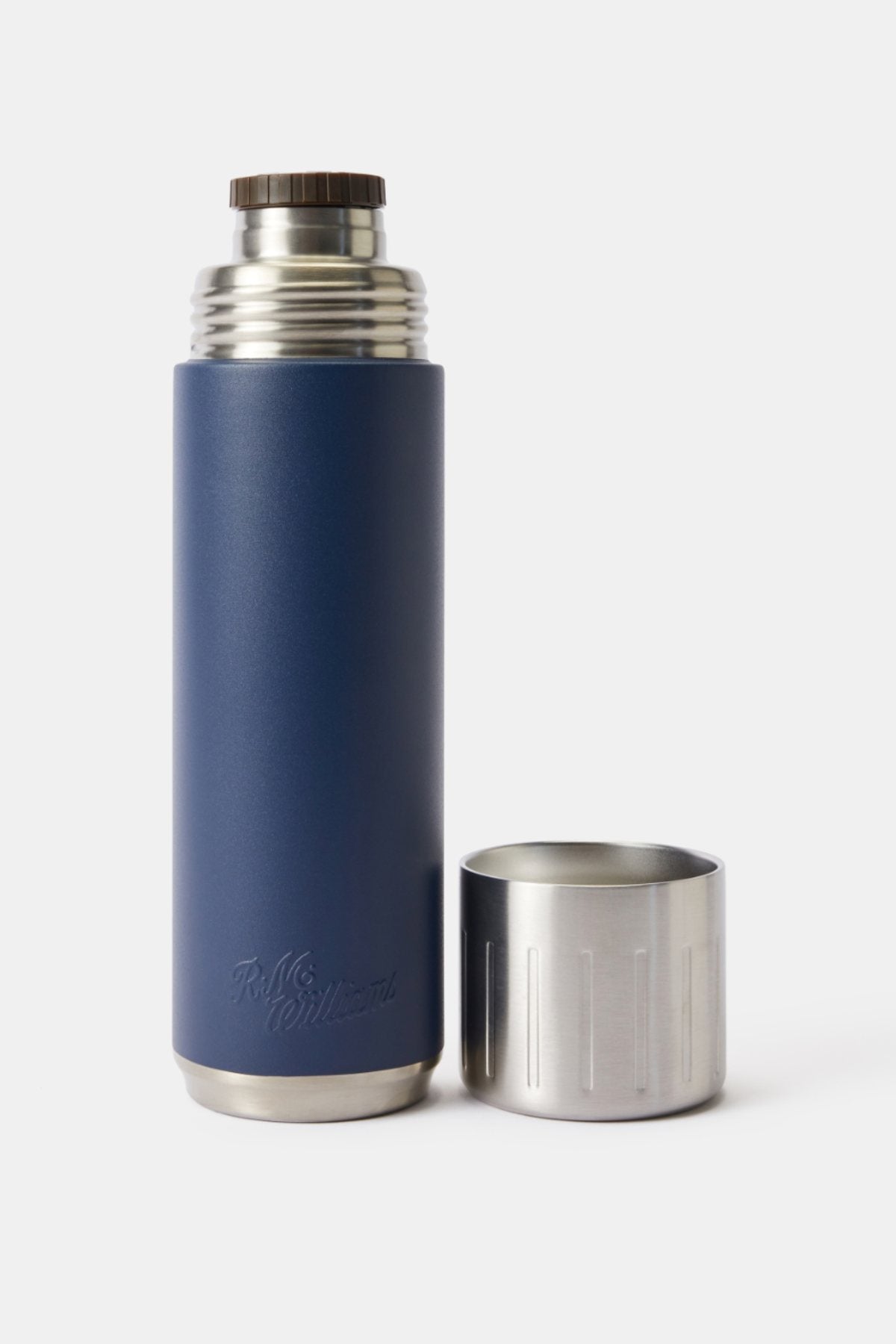 The RM Williams Vacuum Flask, featuring double-wall stainless steel insulation and a navy blue body, stands upright with its metallic screw-on lid placed upside down on a plain white background.