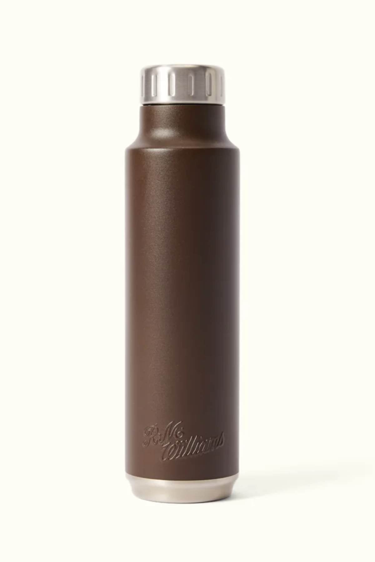 Introducing the RM Williams Water Bottle: a stylish brown stainless steel bottle with a silver cap, featuring a sleek, BPA-free design. Its vacuum-insulated construction ensures your beverages remain at the ideal temperature. The bottle is elegantly finished with an embossed logo at the base, set against a smooth, light surface.