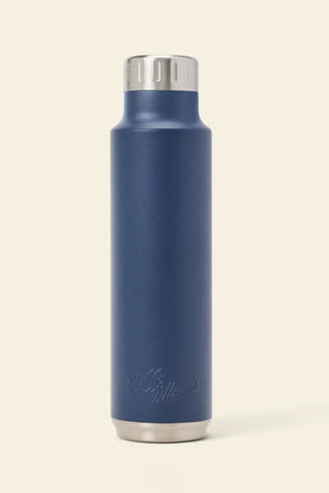 The RM Williams Water Bottle is a tall, navy blue stainless-steel vacuum flask with a silver screw-top lid and base, shown upright on a beige background. Subtle logo engraving near the bottom keeps your drink perfectly hot or cold on any adventure.