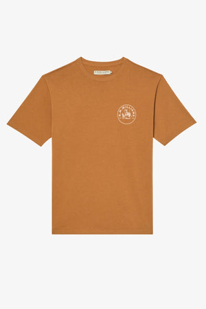 The RM Williams Wondai T-Shirt is a brown, short-sleeve top crafted from lightweight cotton jersey, featuring a minimalist illustration encircled by graphic text and a small white circular logo on the left chest.