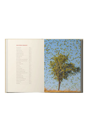 An open, premium hardcover RM Williams Outback Diary 2024 displays a contents list on the left and a striking photo of a tree beneath a blue sky filled with birds in flight on the right, embodying the diary's spirit.