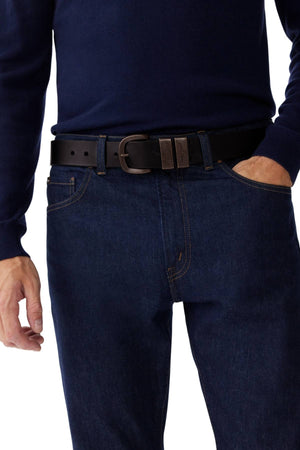 A person wears a navy blue long-sleeve shirt tucked into dark blue jeans with an RM Williams Drover Belt, shown from shoulders to mid-thigh, with one hand resting near a pocket.