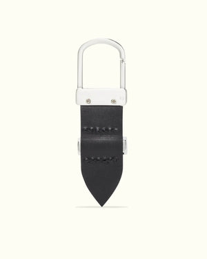 Introducing the RM Williams Drover Key Fob: a sleek keychain featuring a silver carabiner clip on a black double butt leather strap with visible stitching, antique brass hardware, and a pointed end, all against a light gray background for an elegant look.