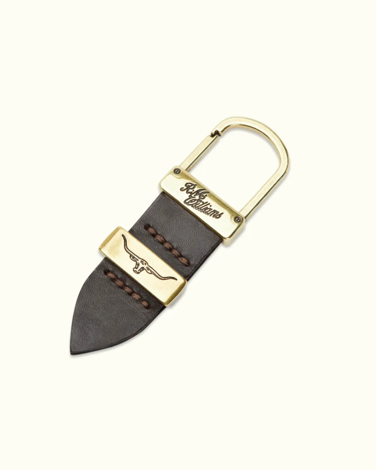 The RM Williams Drover Key Fob features a brass D-ring and dark double butt leather. Its rustic charm is accentuated by antique brass hardware with an engraved longhorn symbol and stitched detailing, while an engraved text on a smaller brass plate adds elegance.