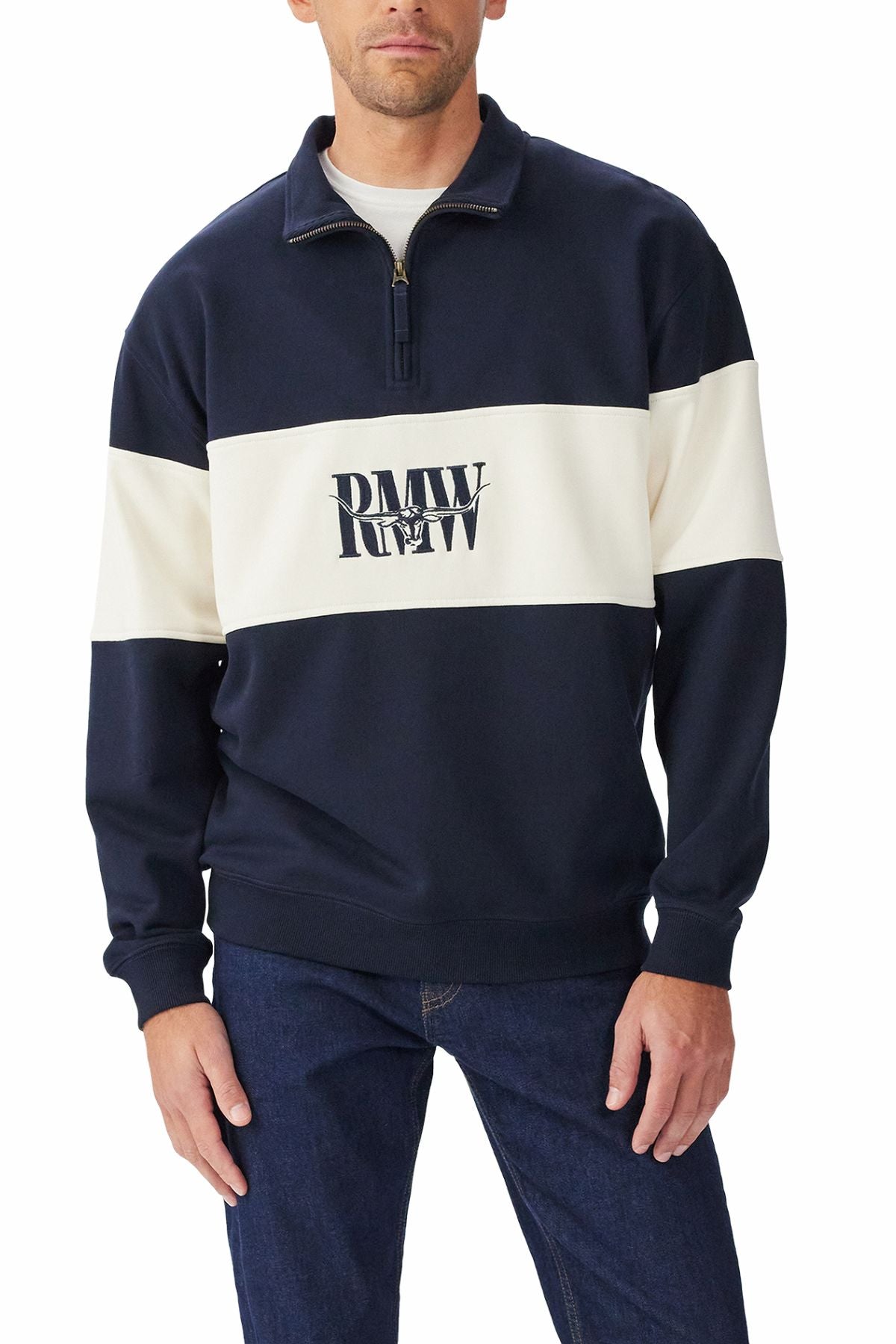 A man wears the RM Williams Heritage 1/4 Zip Sweatshirt in navy with a wide white stripe and "PMW RW" logo on the front, paired with dark blue jeans.