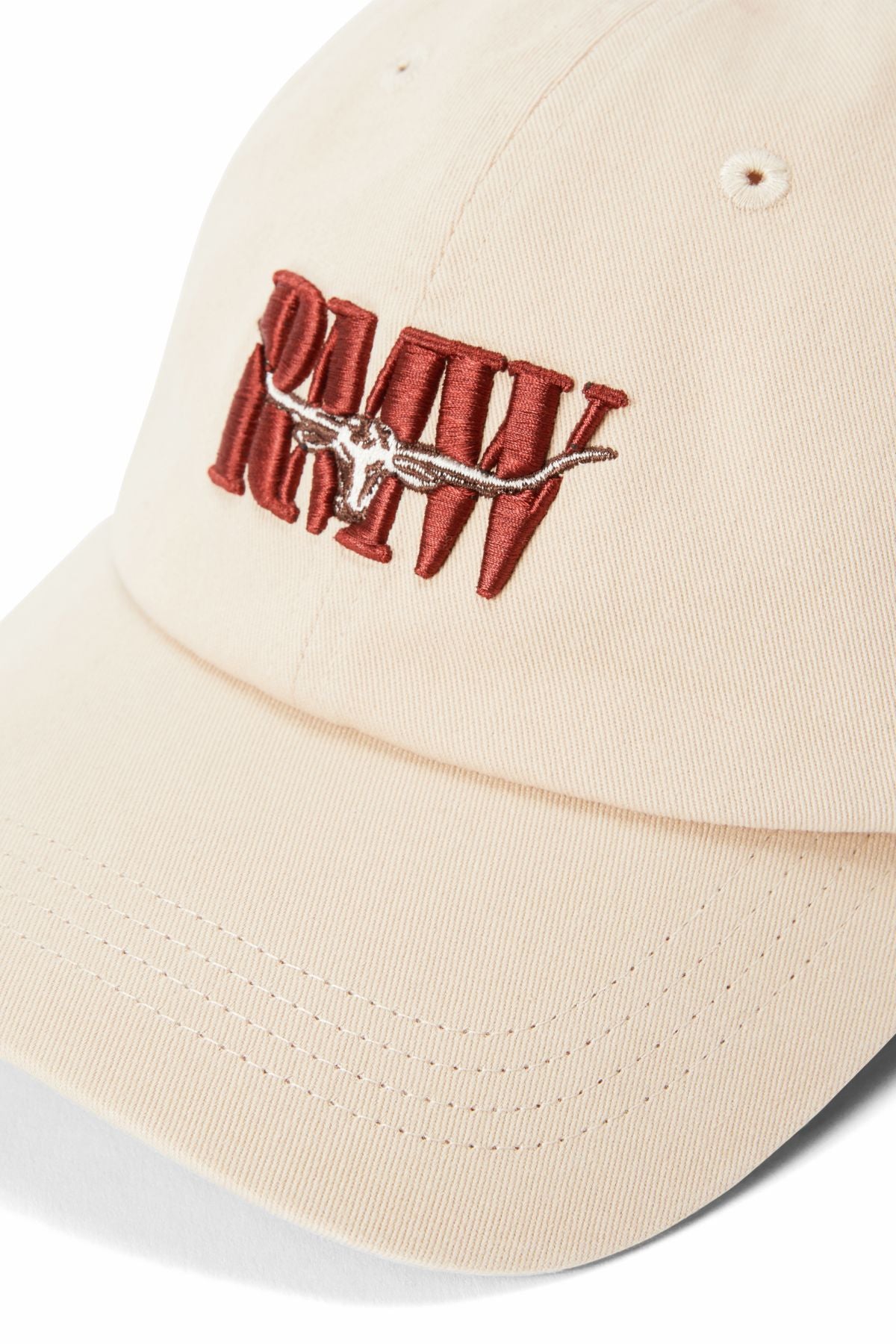 The RM Williams Heritage Twill Cap is a beige organic cotton cap with "RAW" embroidered in bold red, a brown and white steer skull above the text, and an adjustable strap for a custom fit.
