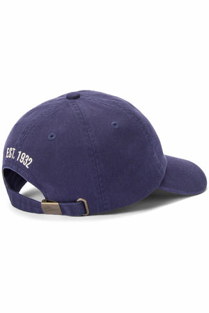 The RM Williams Heritage Twill Cap in navy blue is shown from the back, featuring white "EST. 1932" embroidery above an adjustable strap with a metal buckle.