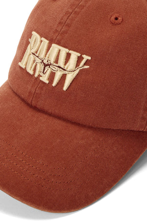 The RM Williams Heritage Twill Cap features a rust hue, classic logo with thick beige "RAW" embroidery—some letters have a streaked effect. Made of durable twill, it offers an adjustable strap for comfort and timeless style with rugged details.